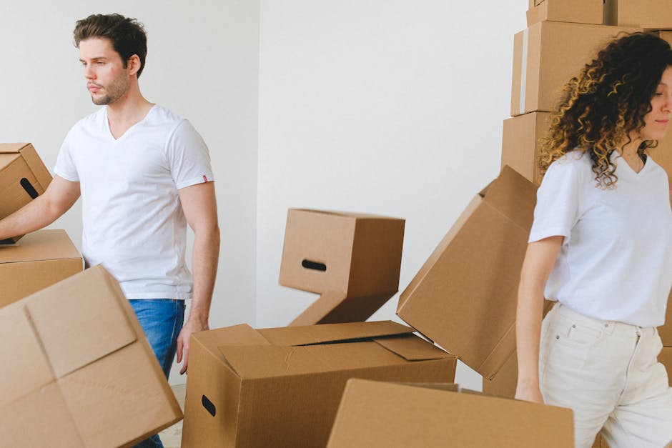 Inside a residential property during a house move, a woman with dark hair, wearing a white top, is seated on the floor and handling packing materials or documents. Behind her, there is a doorway leadi